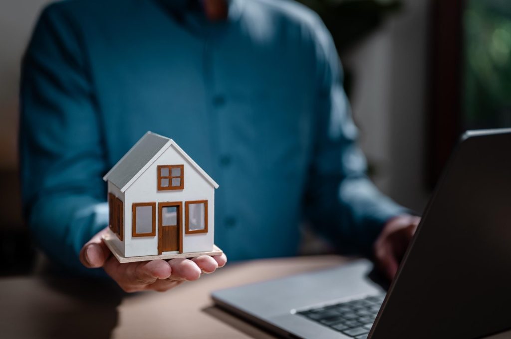 Professional working on laptop while holding miniature house